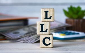 LLC (Limited Liability Company) - acronym on wooden cubes on the background of a cactus and banknotes. Business concept