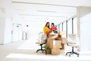 Businesswomen unpacking cardboard boxes in new office